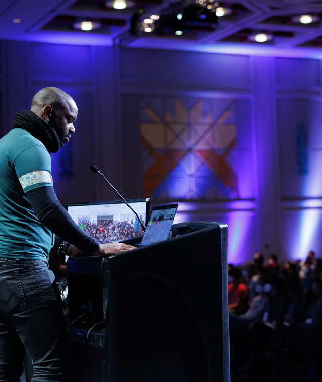 Speaker at a conference with a laptop on a podium and audience in the background