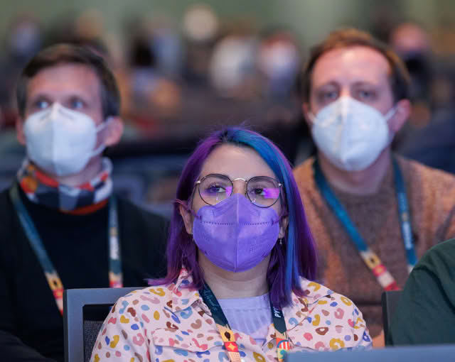 Audience members at a conference, some wearing masks