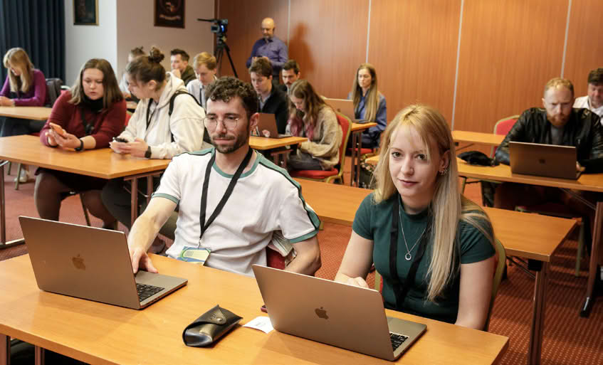 Close-up of a person typing on a laptop with another person writing in a notebook beside them