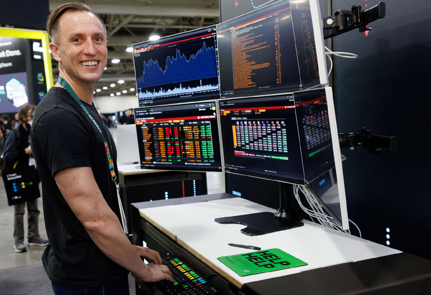 Person smiling in front of multiple computer screens at a conference