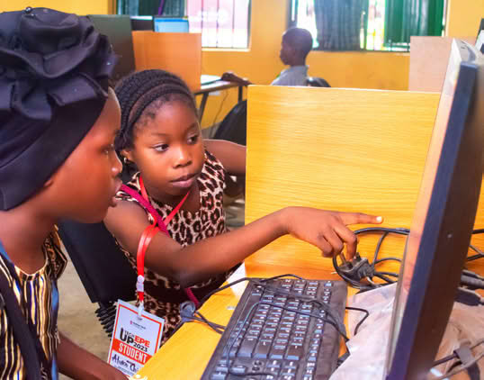 A person teaching a child how to use a computer in a classroom setting