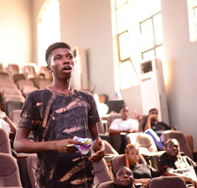 A person standing and speaking in front of an audience in a lecture hall