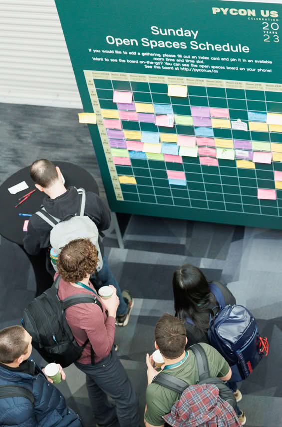 A group of people looking at a board with a schedule for 'PyCon US 2023 Open Spaces'