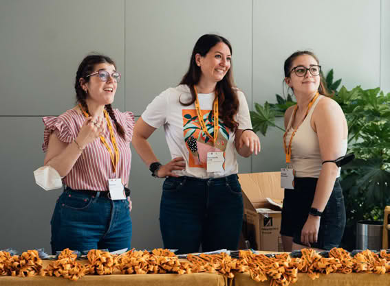 Three people standing behind a table with snacks, smiling and talking